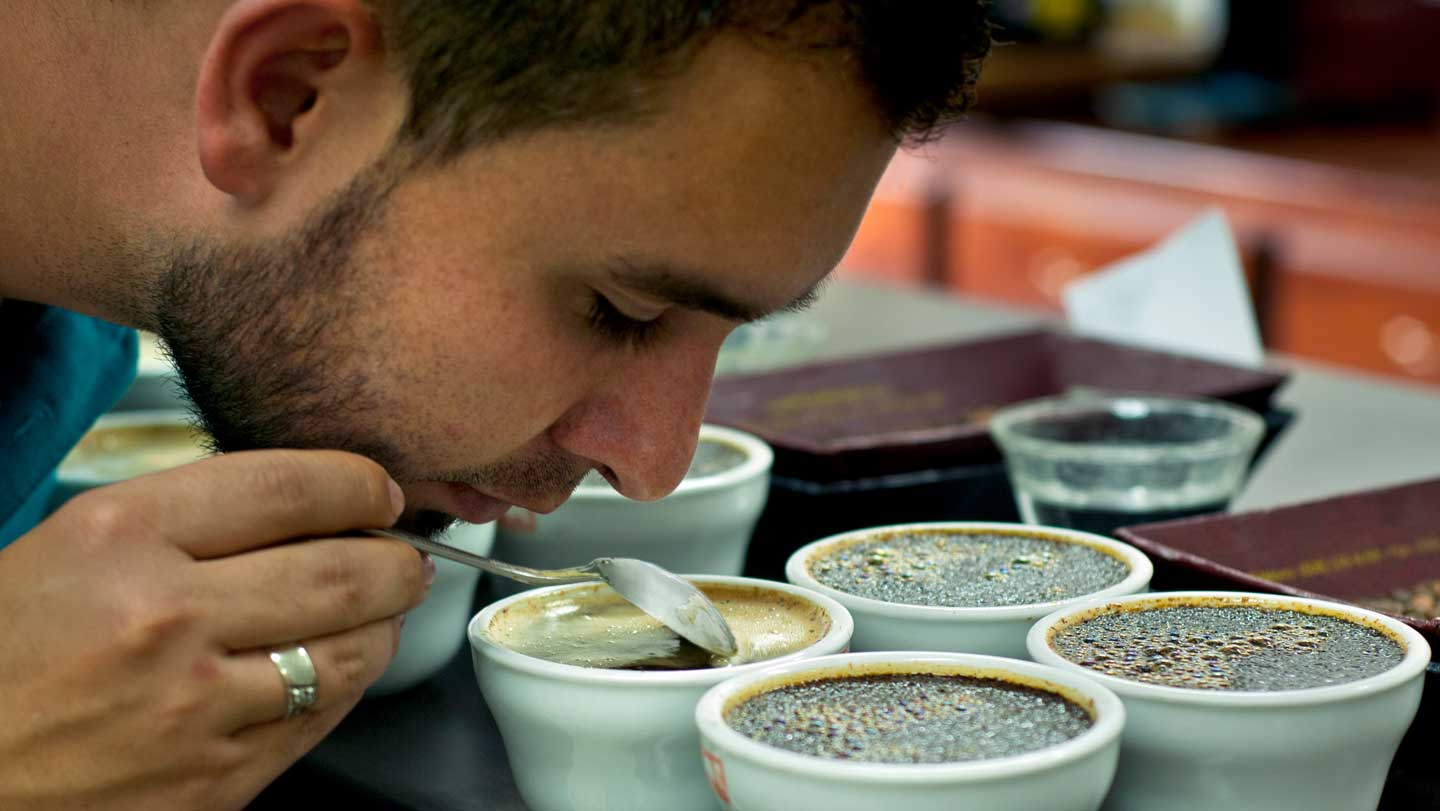 कोविड से संबंधित गंध हानि वर्षों तक बनी रह सकती A man sniffs a cup of coffee while holding a spoon.